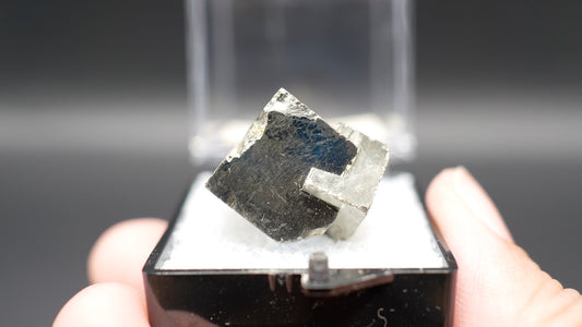 Pyrite mineral sample on a black stand held by a hand with a dark background